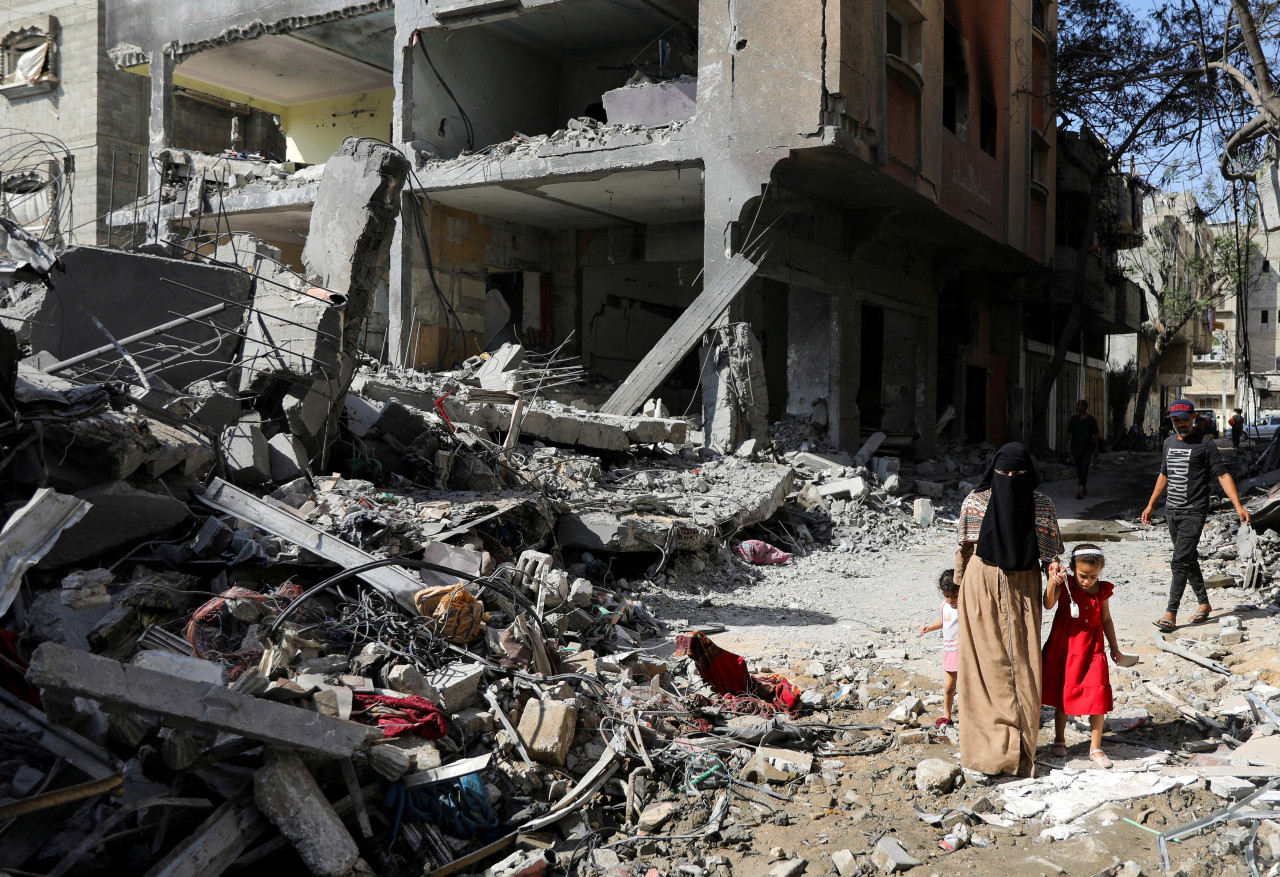 Una mujer y un niño caminan entre escombros tras ataques israelíes en Gaza. Foto: Reuters